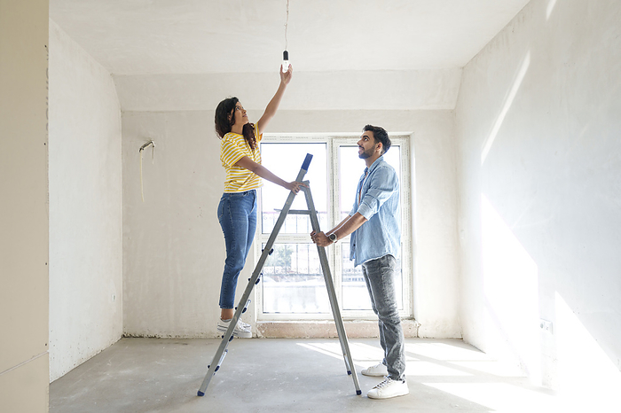 Young couple using ladder and installing light bulb at new home