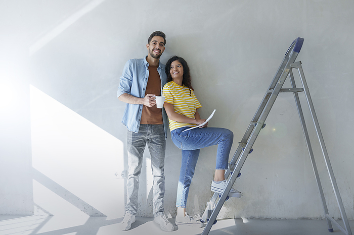 Happy couple standing in front of wall near ladder at new home