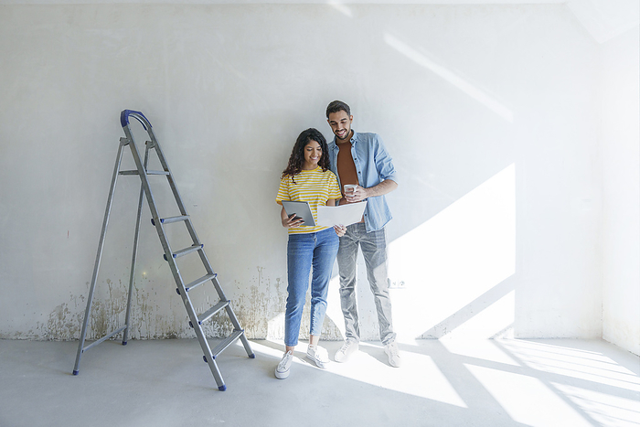 Young couple with tablet PC discussing over blueprint in front of wall