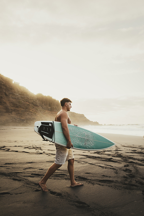 Young man carrying surfboard and walking at beach