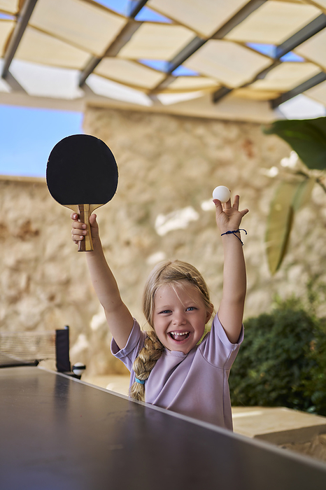 Happy girl cheering with table tennis racket and ball at villa