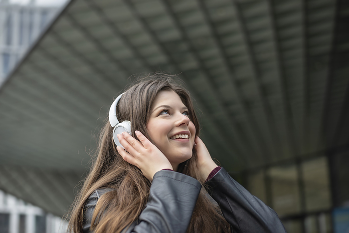 Smiling young woman listening to music through wireless headphones