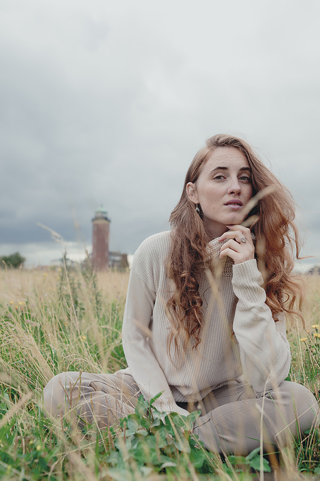 Redhead woman sitting amidst plants in meadow