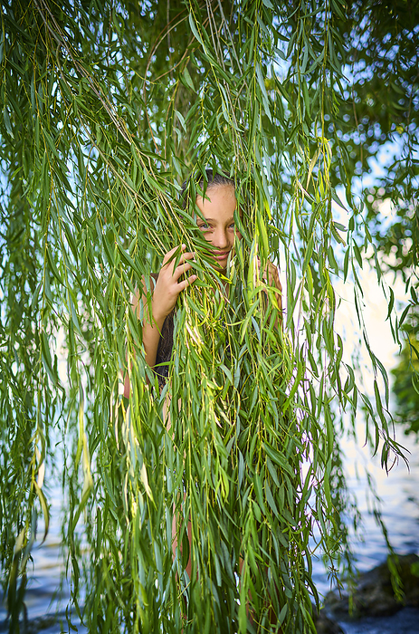 Playful girl hiding behind leaves of willow tree