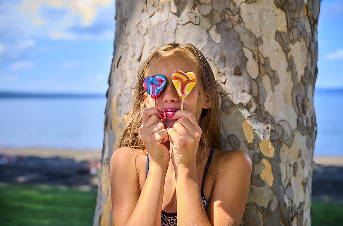 Playful girl holding lollipop over eyes