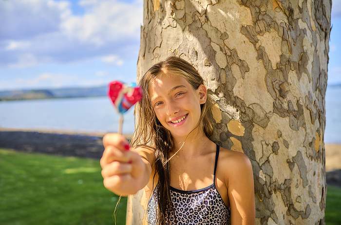 Happy girl holding lollipop near tree trunk