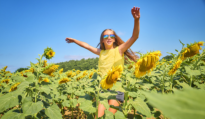 Happy girl wearing sunglasses and dancing in sunflower field