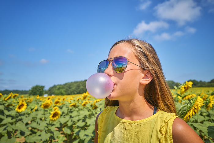 Girl blowing bubble gum in sunflower field on sunny day