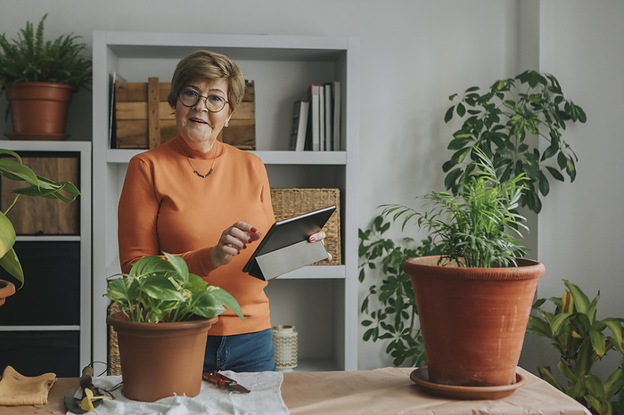 Smiling woman holding tablet PC with plants on table at home