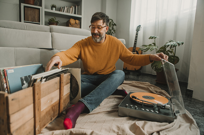 Man listening to vinyl records sitting with box full of disks at home