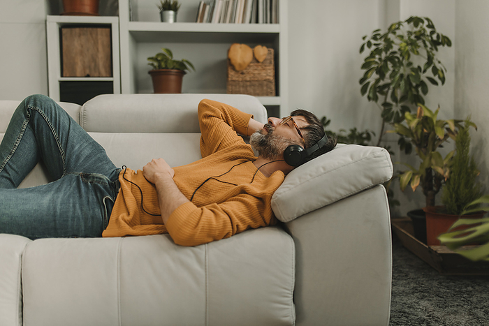 Man listening to music through headphones lying on sofa in living room at home