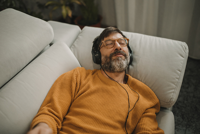 Man listening to music through headphones lying on sofa at home