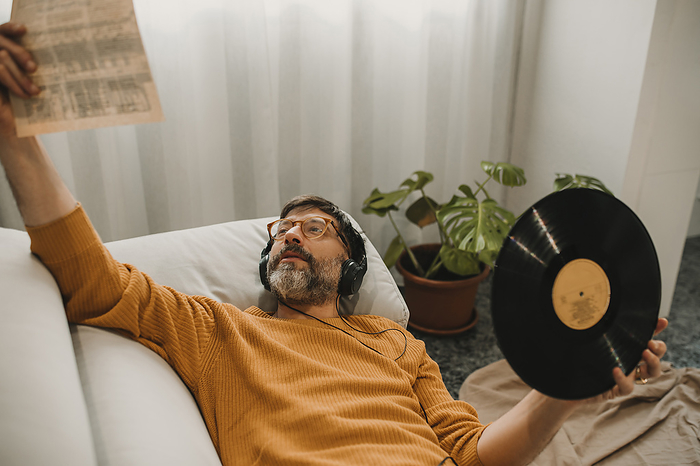 Man listening to music and reading vinyl paper holding record at home