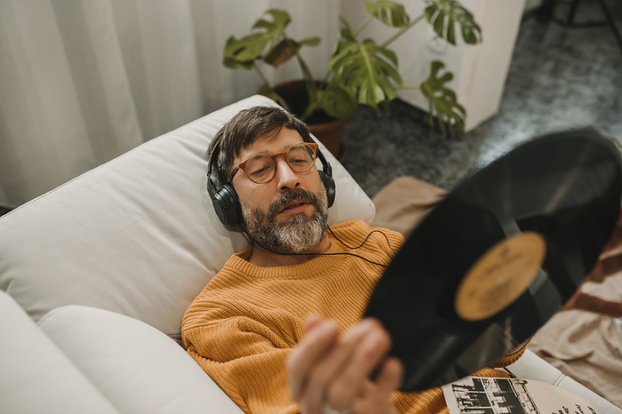 Man listening to music and looking at vinyl lying on sofa