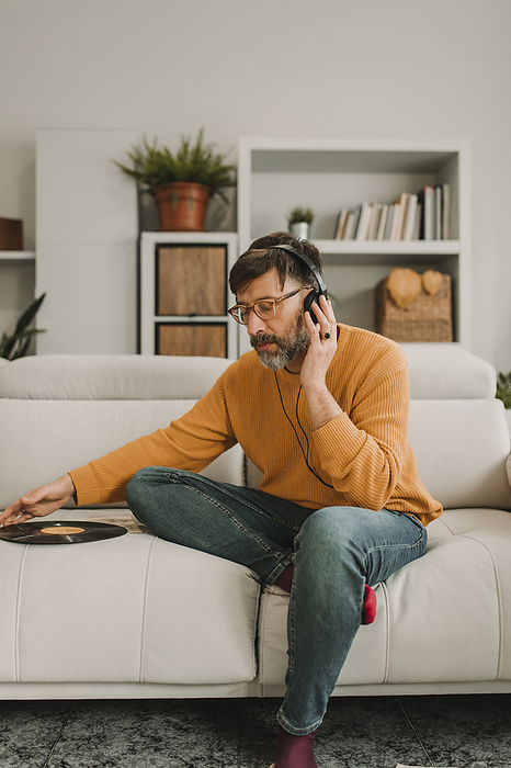 Man listening to music through headphones sitting with vinyl on sofa at home