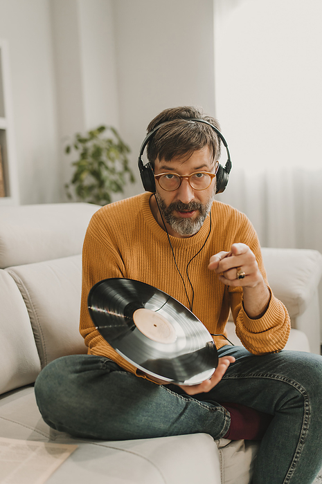 Man listening to music through headphones sitting with record on sofa at home