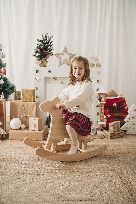 Smiling cute blond girl sitting on rocking horse at home