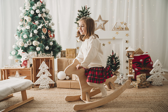 Happy girl sitting on wooden rocking horse at home
