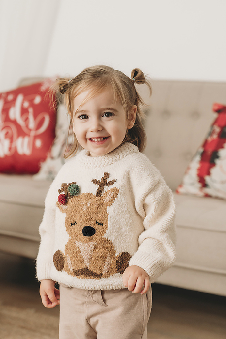 Smiling cute girl wearing Christmas sweater near sofa at home