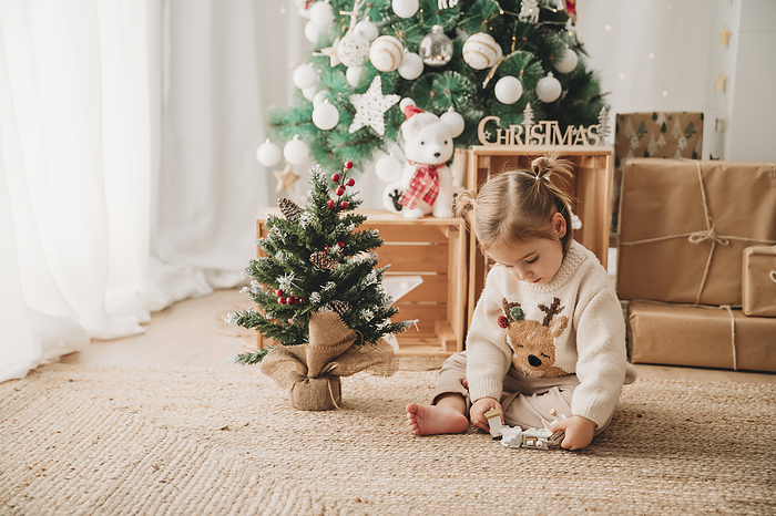 Girl playing with Christmas decoration near tree at home