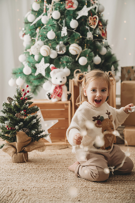 Happy girl playing near Christmas trees at home