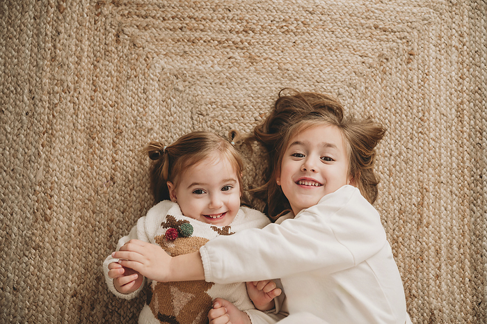 Happy sisters lying on carpet at home