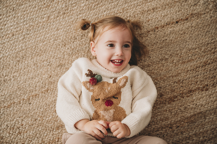 Smiling girl wearing Christmas sweater and lying on carpet at home