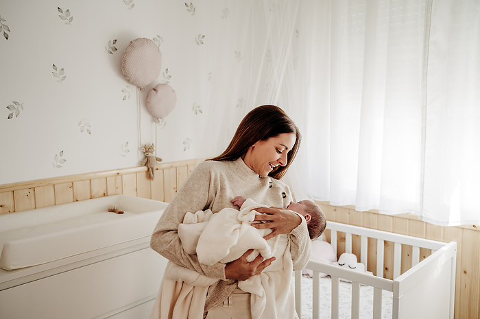 Happy mother holding baby girl in arms near crib at home