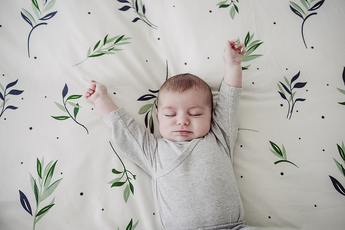 Cute baby girl stretching arms lying in bed at home