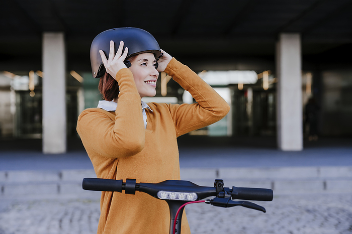 Smiling woman wearing helmet and standing with electric push scooter