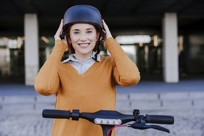 Smiling woman wearing helmet and standing near building