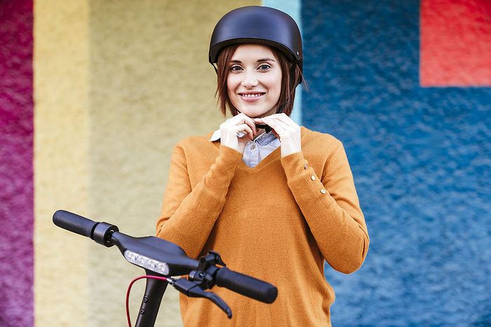 Smiling woman adjusting helmet in front of multi colored wall