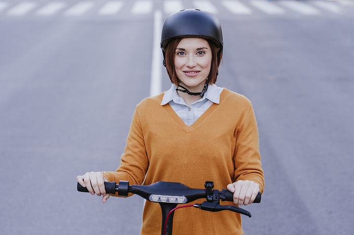 Smiling woman standing with electric push scooter on road