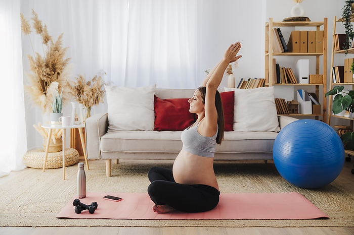 Pregnant woman practicing yoga with arms stretched on exercise mat at home