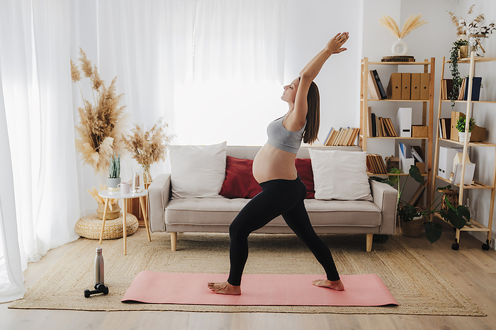 Pregnant woman practicing yoga on mat in living room at home