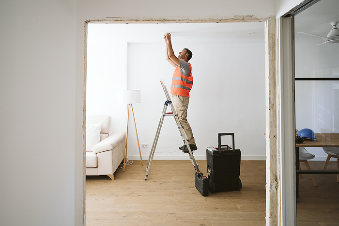 Repairman standing on ladder and working in house under renovation