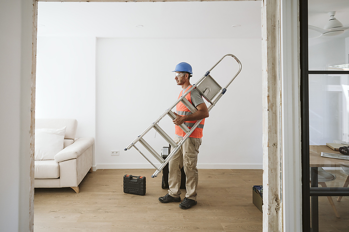 Maintenance engineer carrying ladder in house under renovation