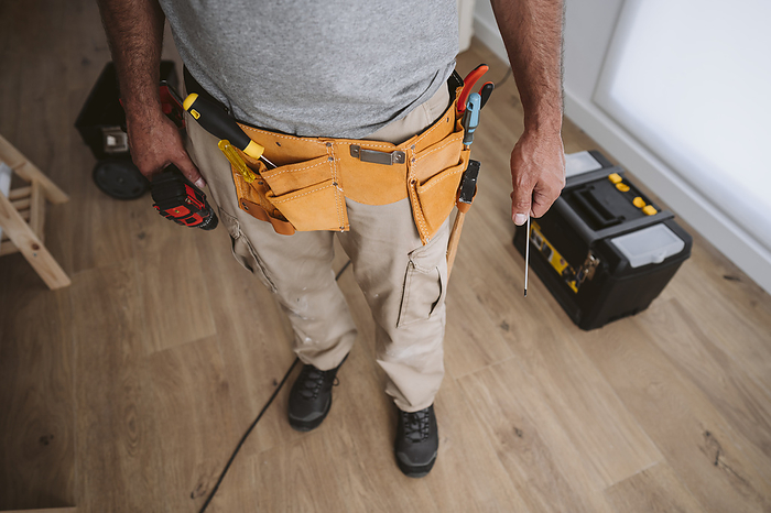 Repairman wearing tool belt and standing at home