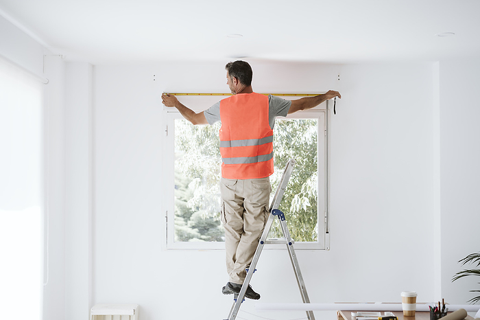 Mature repairman measuring window in house under renovation