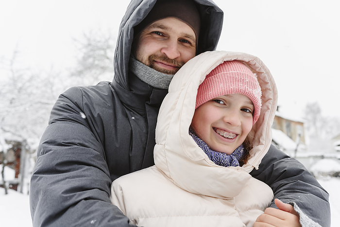 Smiling father embracing daughter in winter