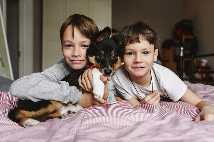 Brothers lying with dog on bed