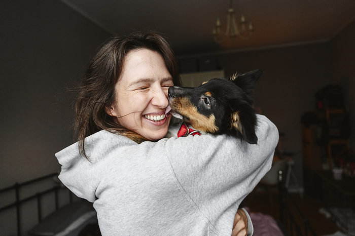 Happy woman with eyes closed holding dog at home