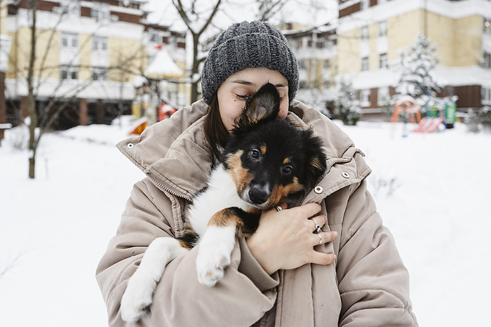 Woman covering dog with winter jacket on snow