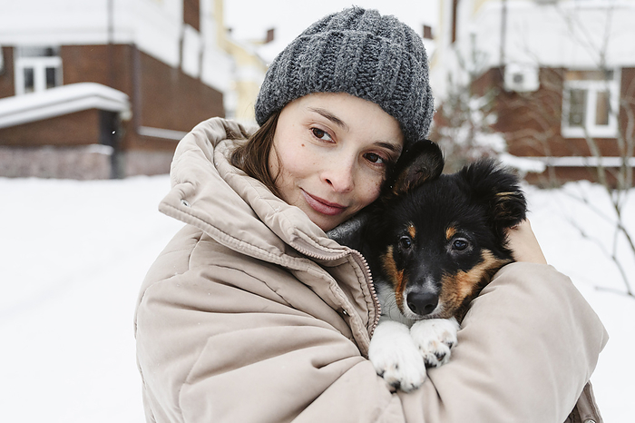 Woman wearing knit hat and embracing dog in winter
