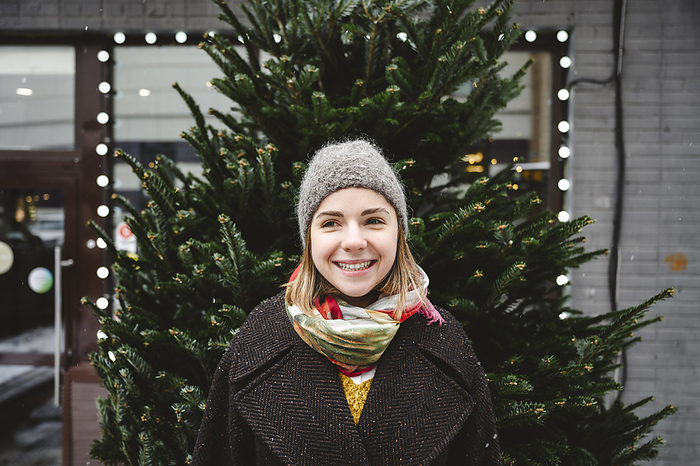 Happy young woman standing in front of Christmas tree