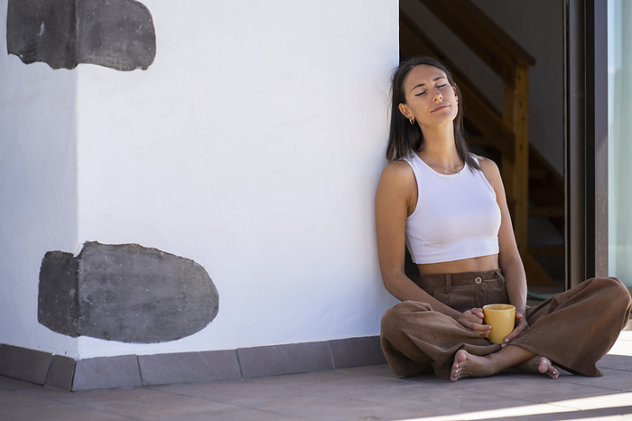 Woman holding mug and sitting with eyes closed at front porch