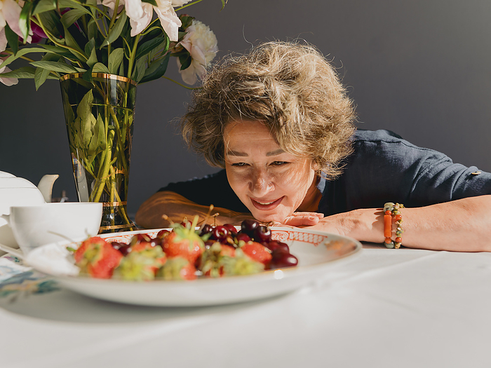 Smiling woman looking at berries in plate on table at home