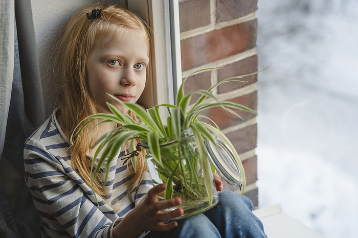 Girl holding spider plant and sitting near window