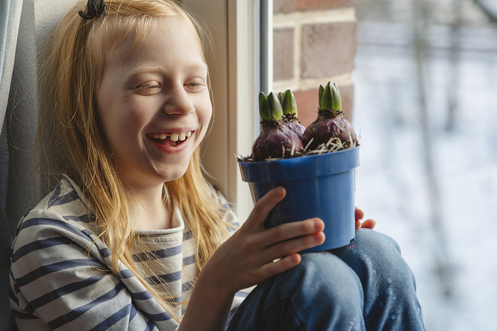 Happy girl holding hyacinth bulbs and sitting near window