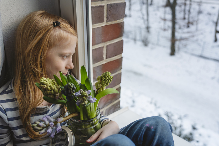 Girl holding bunch of hyacinth flowers in jar and sitting near window